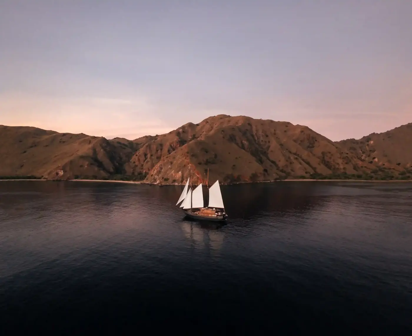 Small phinisi anchored in a bay below hills