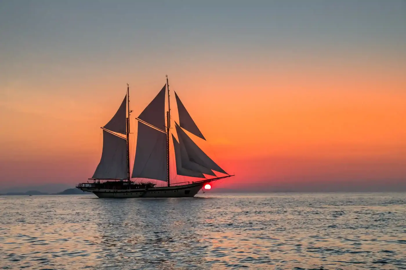 Phinisi silhouette under sail against a red sky