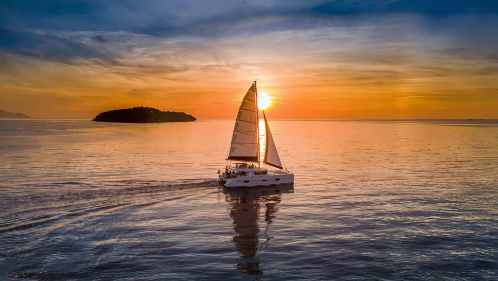 Catamaran sailing towards the sunset past a small island