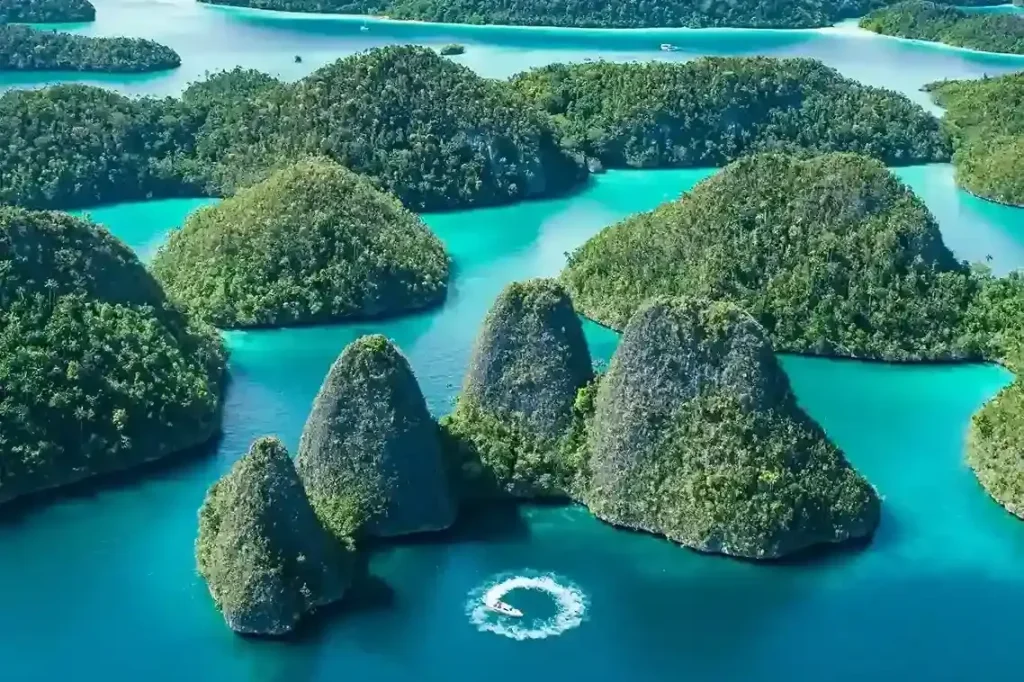 Aerial view of a boat crossing a lagoon among forested karst islets