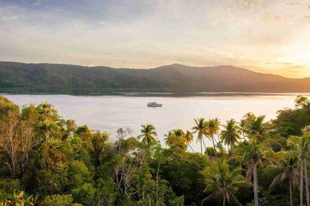 Sunset over a palm-fringed bay with a boat at anchor
